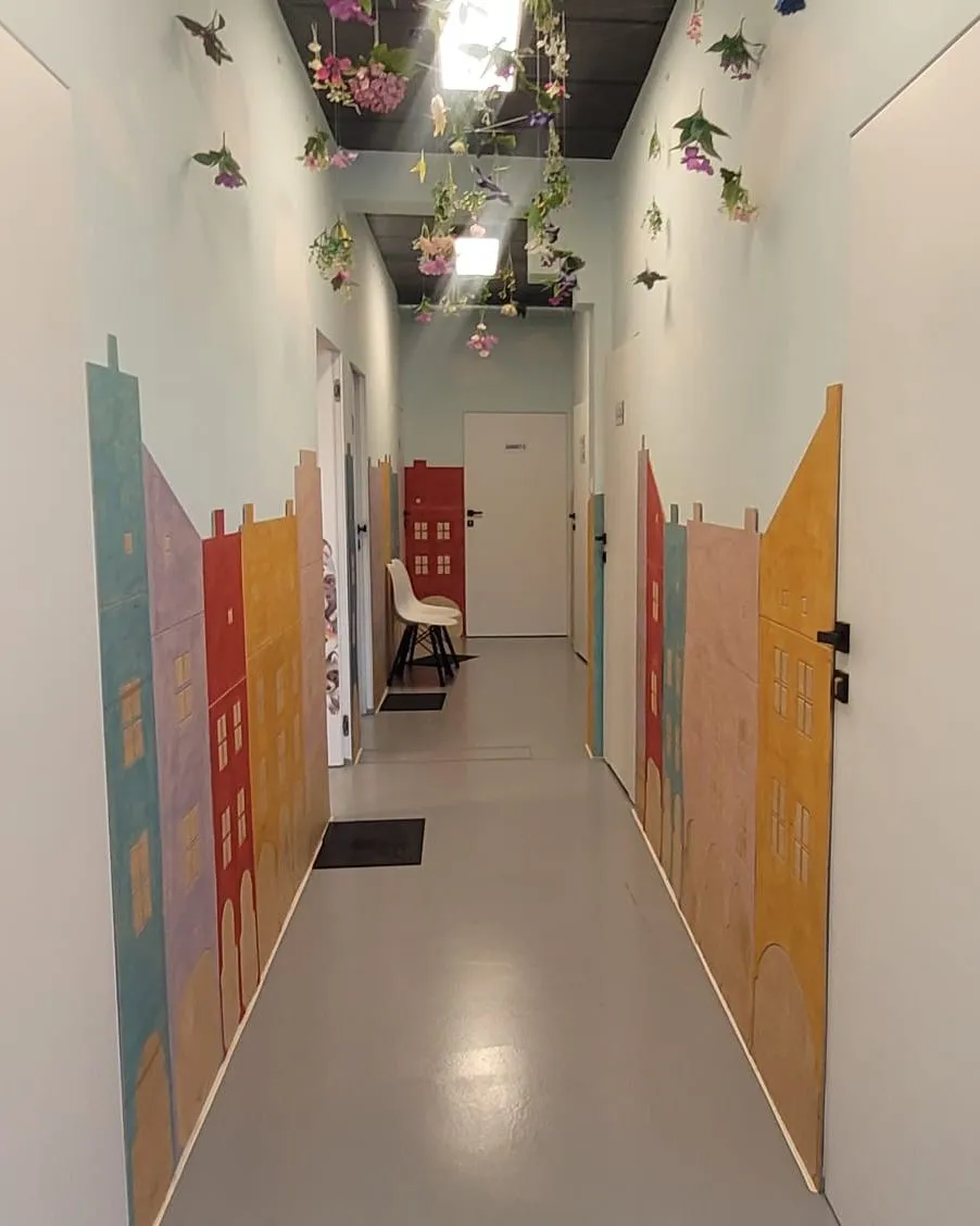 Kolorowy korytarz PoMocne Centrum Terapii z drewnianymi kamieniczkami na ścianach i kwiatami pod sufitem